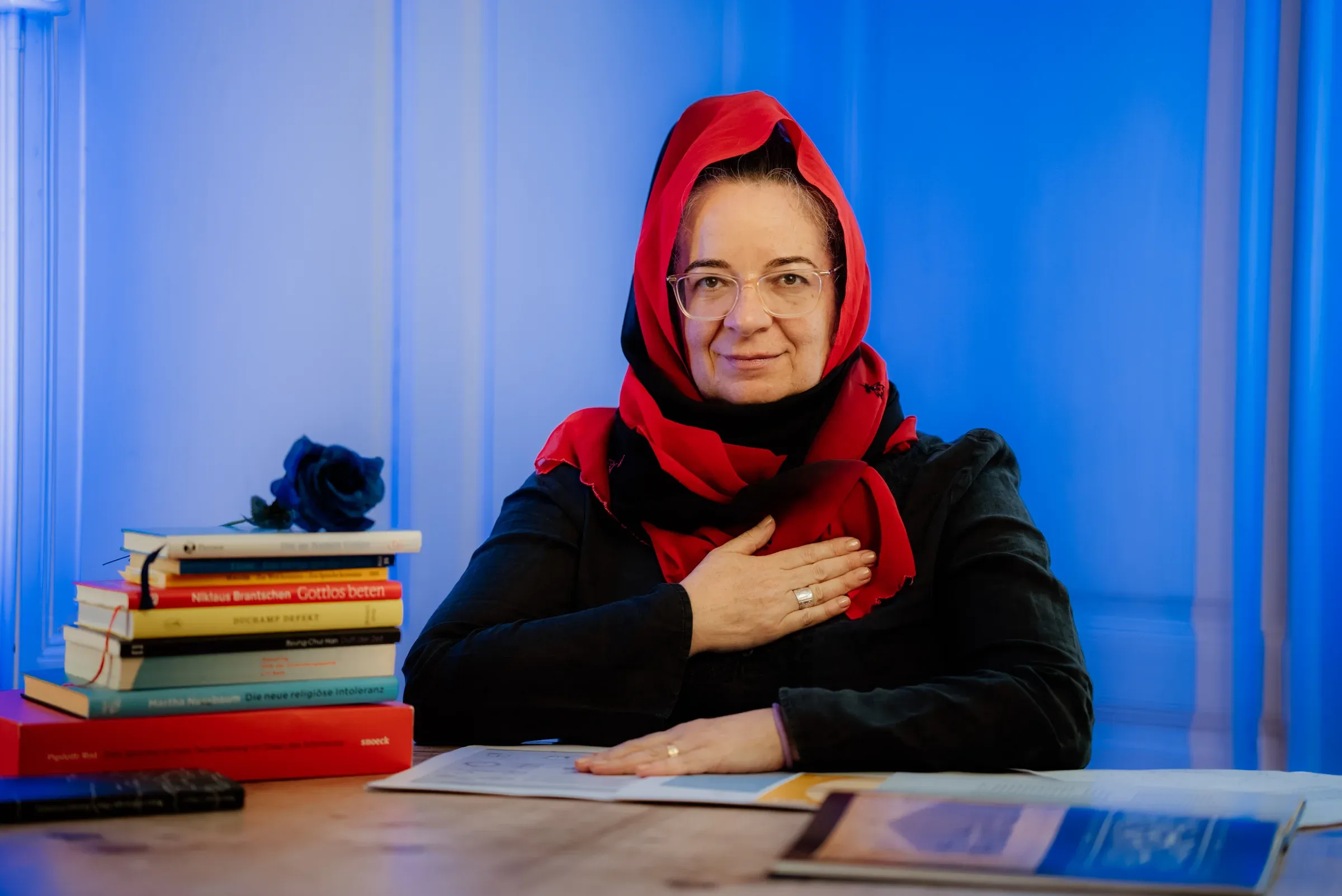 Pfarrerin Kathrin Rehmat am Set von Hä? Gott! vor blauer Wand mit Bücherstapel
